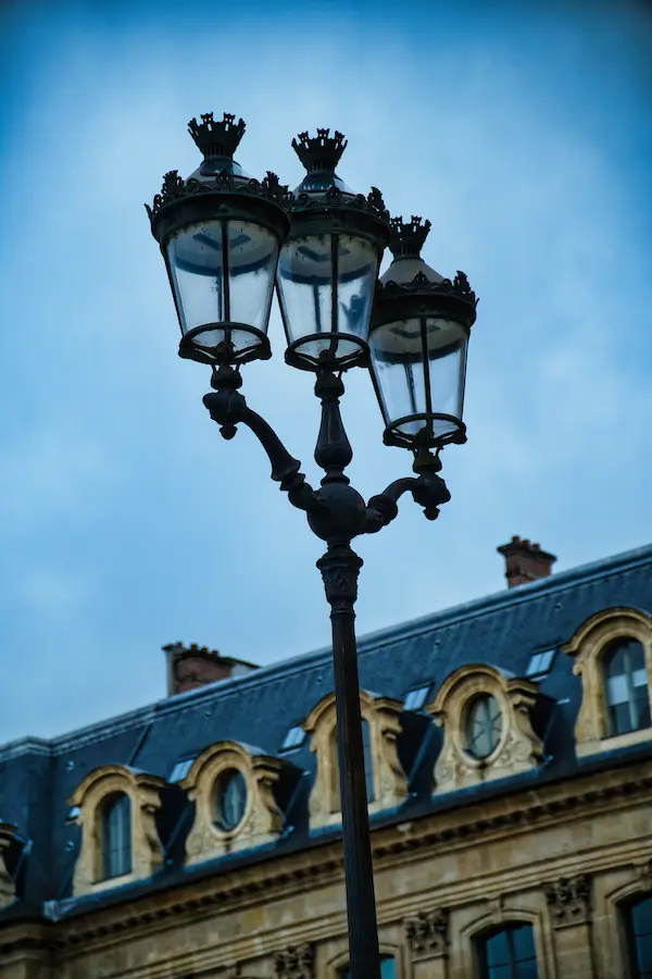 Réverbère parisien à trois lanternes ornementées se détachant sur fond de façade haussmannienne aux lucarnes ouvragées