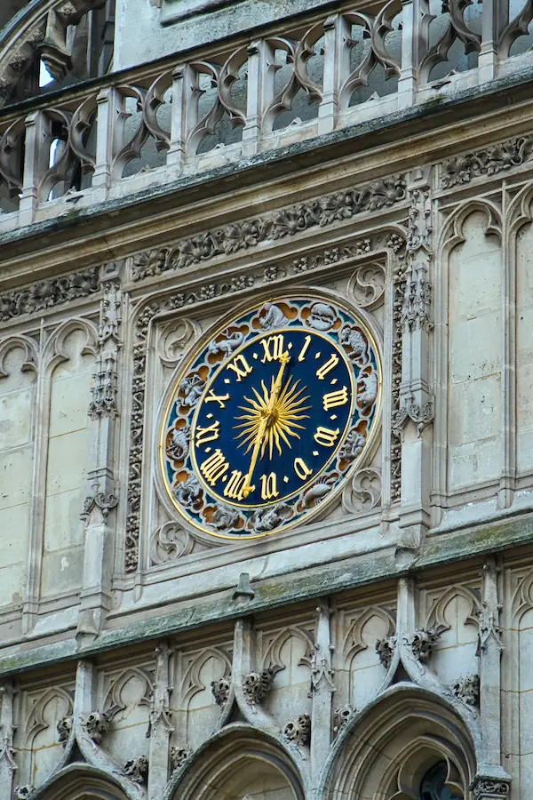 Horloge gothique ornementée au cadran bleu nuit et chiffres romains dorés, enchâssée dans une façade de pierre sculptée avec détails architecturaux médiévaux
