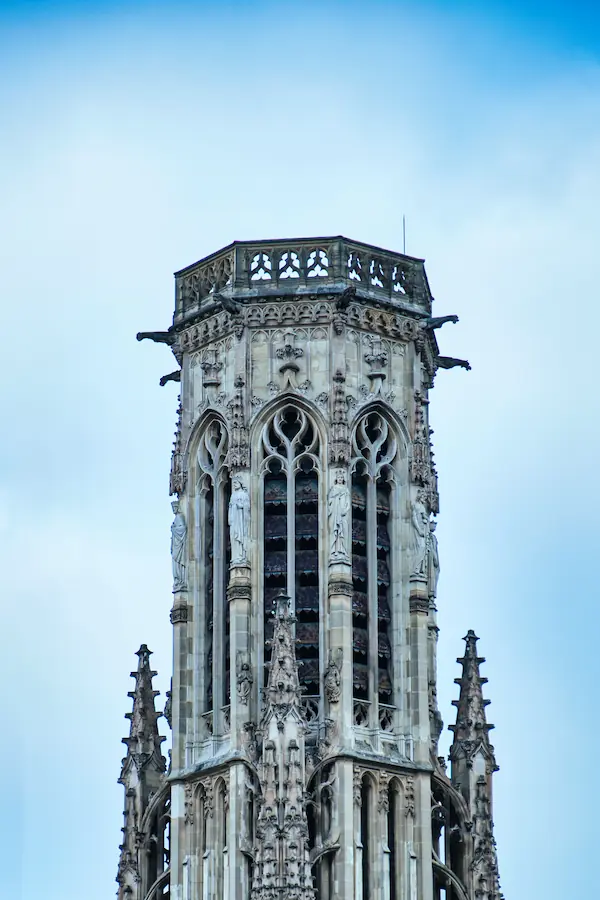 Tour gothique en pierre sculptée ornée de statues de saints, de gargouilles et de pinacles, avec fenêtres à meneaux et balustrade ajourée au sommet