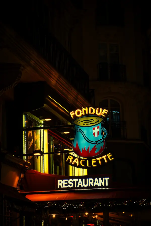 Enseigne lumineuse nocturne d'un restaurant de fondue et raclette, avec un caquelon bleu turquoise aux couleurs suisses illuminé en néon