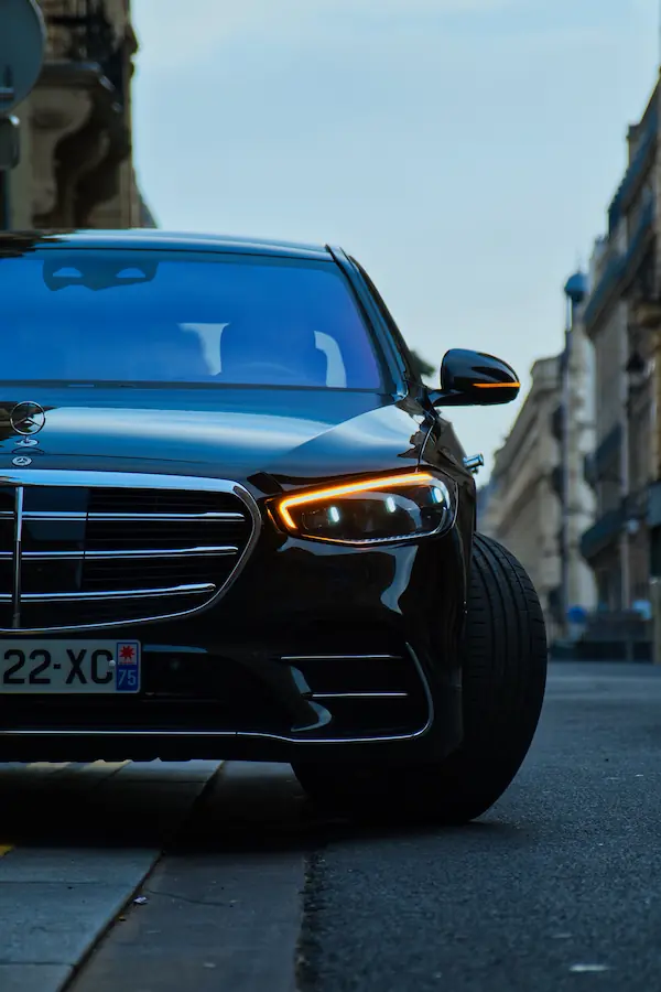 Gros plan sur l'avant d'une Mercedes-Benz Classe S noire, mettant en valeur sa signature lumineuse LED et sa calandre chromée, photographiée dans une rue parisienne