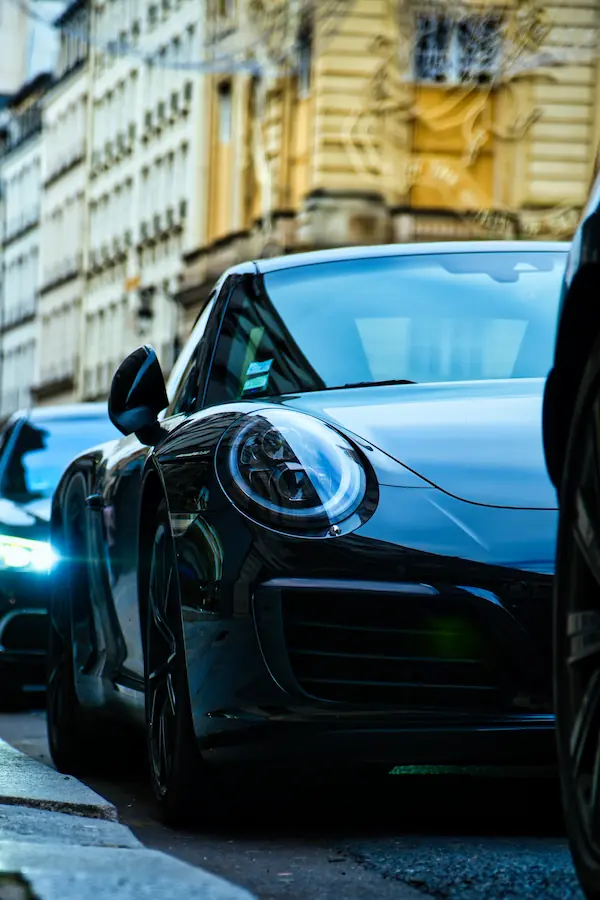 Gros plan sur le phare avant et l'aile d'une Porsche 911 noire garée dans une rue parisienne, mettant en valeur ses lignes iconiques et son design caractéristique