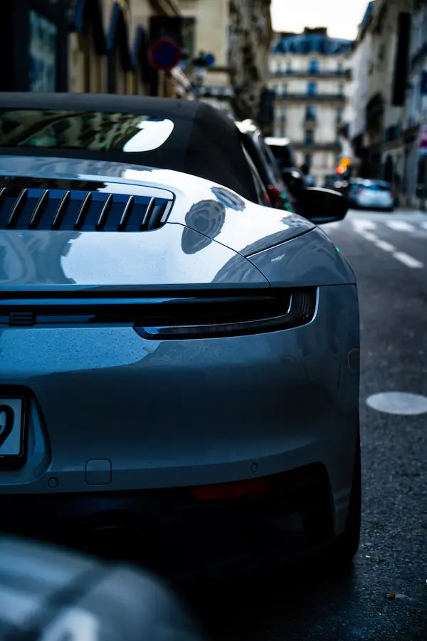 Détail de l'arrière d'une Porsche 911 grise, mettant en évidence ses lignes fluides, sa grille d'aération et son capot moteur caractéristique, photographiée dans une rue parisienne