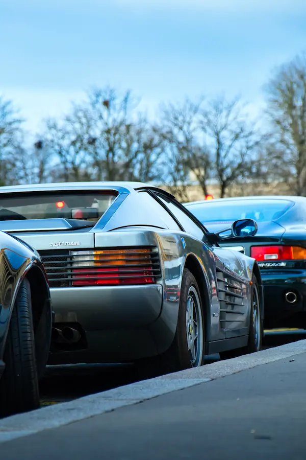 Détail de l'arrière d'une Ferrari Testarossa grise, mettant en valeur ses iconiques grilles latérales et feux arrière horizontaux, caractéristiques du design Pininfarina des années 80