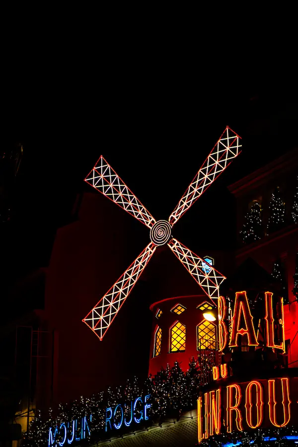 Façade illuminée du Moulin Rouge la nuit, avec son emblématique moulin à ailes rouges lumineuses et ses enseignes au néon, symbole iconique du quartier de Pigalle à Paris