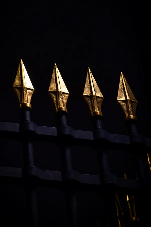 Pointes dorées géométriques d'une grille ornementale parisienne photographiées de nuit, créant un motif répétitif de flèches métalliques sur fond sombre