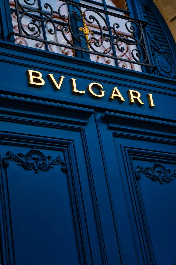 Façade de la boutique Bulgari avec son enseigne lumineuse dorée, ornée de boiseries bleues sculptées et d'une grille en fer forgé aux motifs floraux avec fleur de lys dorée