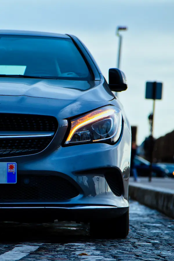 Gros plan sur le phare LED et la calandre d'une Mercedes-Benz Classe A moderne, montrant sa signature lumineuse distinctive et ses détails de design avant sur fond de pavés parisiens