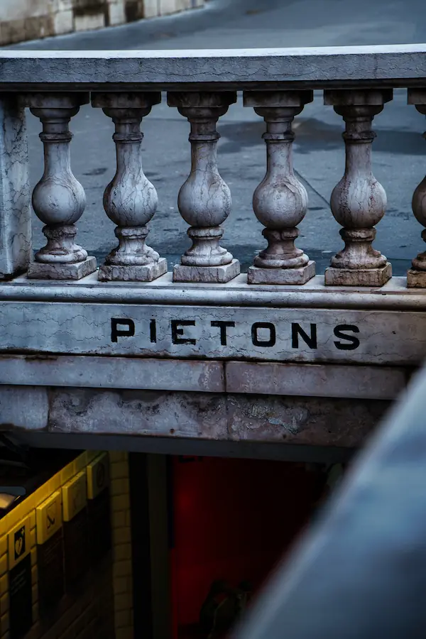 Balustrade en pierre avec colonnes tournées et inscription "PIETONS" gravée, typique des entrées de passages piétons parisiens