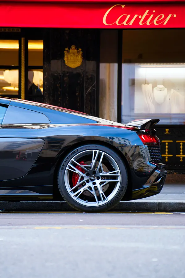 Détail du profil arrière d'une Audi R8 noire stationnée devant une boutique Cartier, montrant la jante en alliage à branches multiples avec étrier de frein rouge.