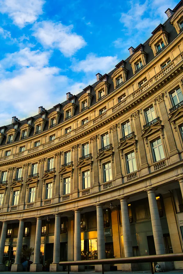 Façade incurvée d'un immeuble haussmannien avec colonnade au rez-de-chaussée, photographiée en contre-plongée au lever du soleil.