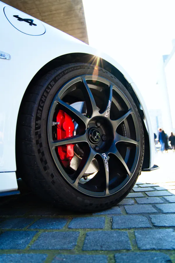 Gros plan sur la roue avant d'une Alpine A110 blanche, montrant la jante en alliage gris anthracite à huit branches, l'étrier de frein rouge et le pneu Michelin.
