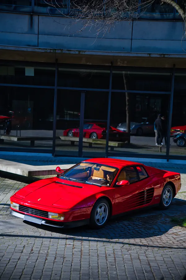 Ferrari Testarossa rouge photographiée de trois-quarts avant, montrant son design iconique des années 80 avec ses prises d'air latérales à lamelles, son capot plat et ses jantes à cinq branches caractéristiques.