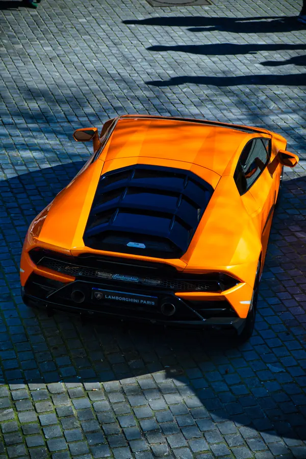 Vue plongeante sur l'arrière d'une Lamborghini Huracán orange, montrant son capot moteur vitré à lamelles, son diffuseur arrière.