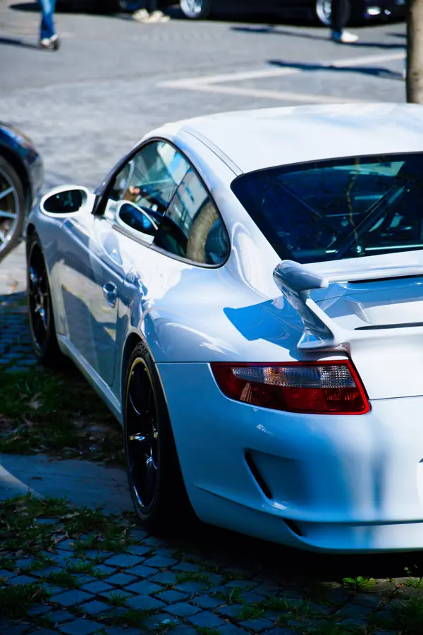 Arrière d'une Porsche 911 GT3 blanche stationnée sur des pavés, montrant son aileron caractéristique et ses feux arrière rouges.