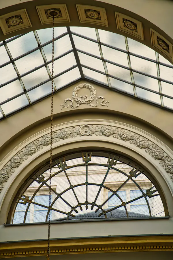 Élément architectural d'une galerie avec verrière en demi-cercle ornée de motifs en couronne, encadrée par des arches décoratives en stuc avec guirlandes florales et une couronne de laurier au sommet.