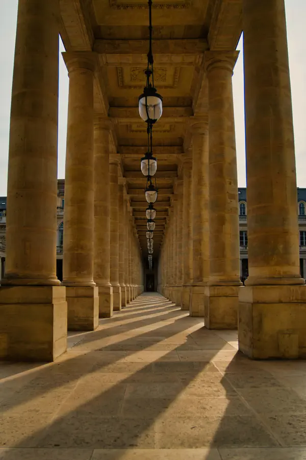 Colonnade majestueuse du Palais-Royal à Paris, avec perspective en enfilade de colonnes dorées créant un jeu d'ombres géométriques au sol.
