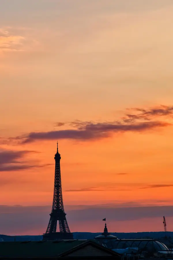 Silhouette de la Tour Eiffel se détachant sur un ciel crépusculaire aux teintes orange et rose.