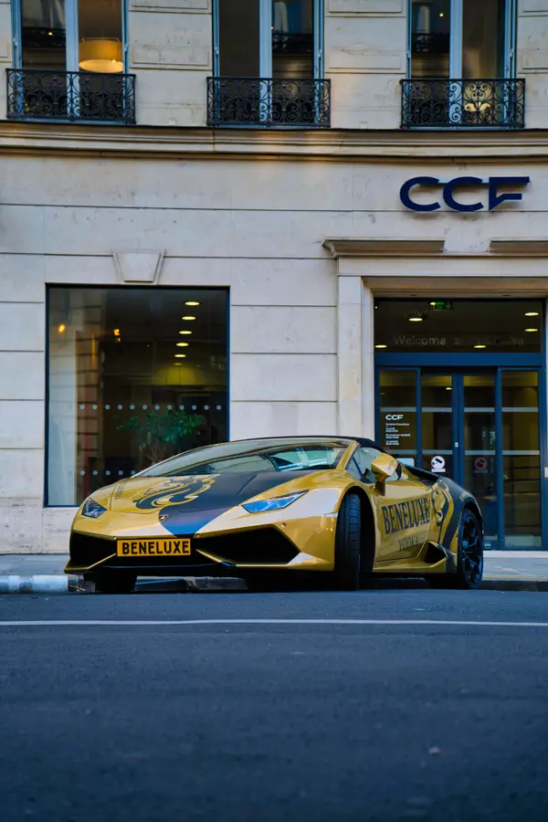 Lamborghini Huracán décapotable jaune avec inscription "BENELUXE" sur la carrosserie, stationnée devant un immeuble parisien avec façade en pierre.