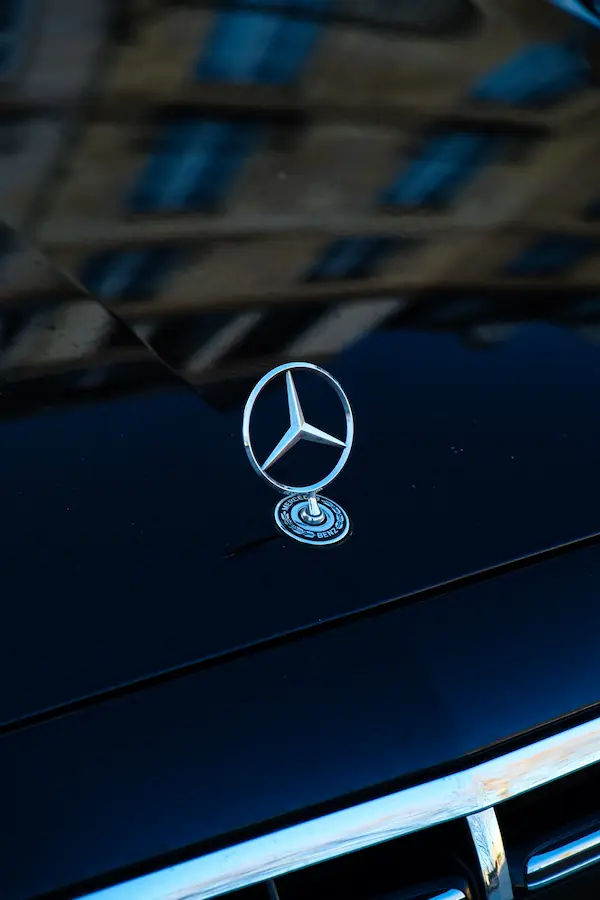 Emblème étoilé Mercedes-Benz chromé sur son socle, photographié en gros plan sur le capot noir brillant d'une voiture, symbole iconique du luxe automobile allemand