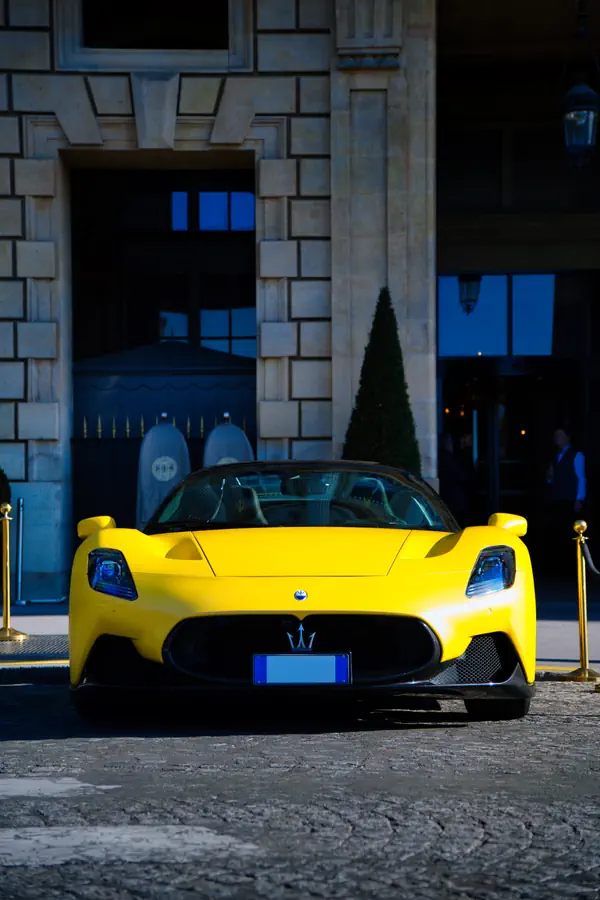 Maserati MC20 jaune photographiée de face devant l'entrée d'un hôtel de luxe parisien, montrant sa calandre noire avec l'emblème du trident, ses phares LED caractéristiques et sa carrosserie aérodynamique.