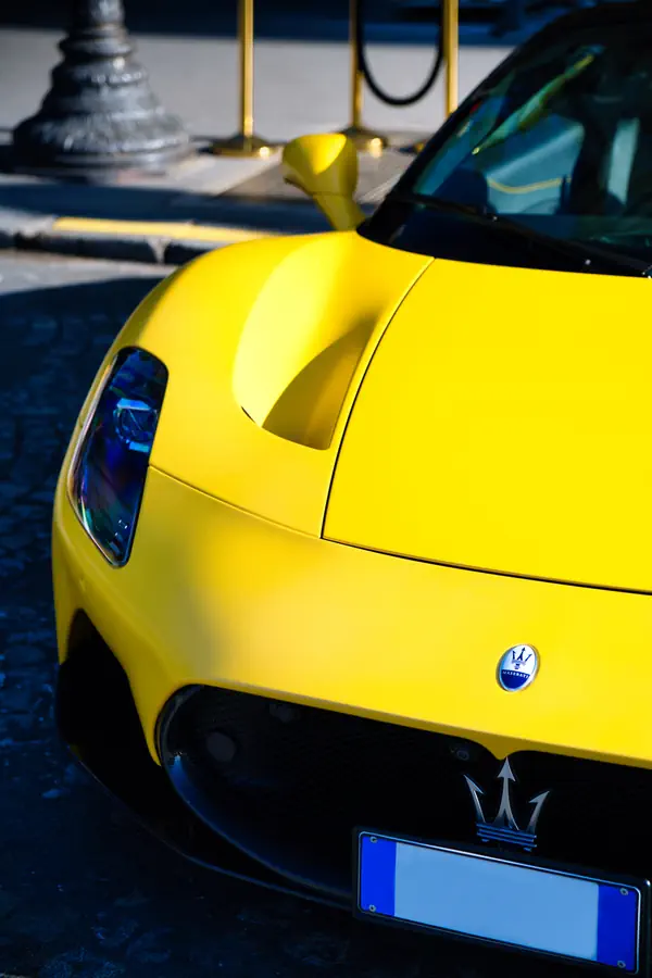 Gros plan sur l'avant d'une Maserati MC20 jaune vif, montrant le détail du phare LED, l'emblème du trident Maserati sur la calandre noire et sur le capot et les lignes sculpturales de la carrosserie.