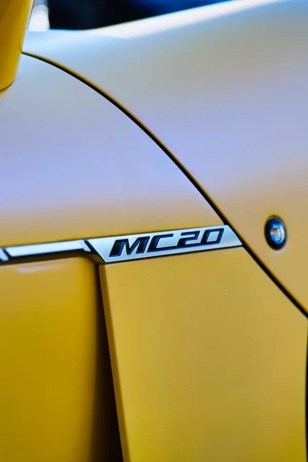Gros plan sur le badge "MC20" en métal chromé apposé sur la carrosserie jaune vif d'une Maserati, montrant les lignes épurées et les courbes élégantes de la portière.