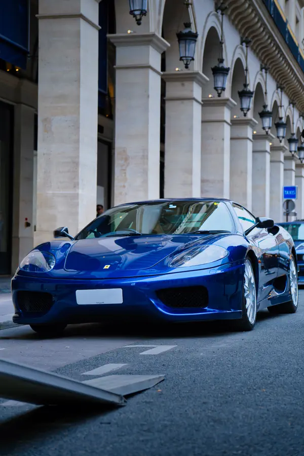 Ferrari 360 Modena bleu métallisé photographiée de face devant les arcades de la place Vendôme à Paris.