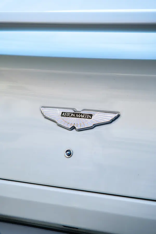 Emblème Aston Martin en forme d'ailes déployées chromées et émaillées sur la carrosserie blanche d'une Vanquish.