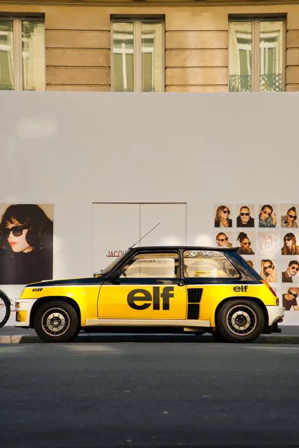 Renault 5 Turbo aux couleurs emblématiques jaune et noire du sponsor Elf, stationnée devant une boutique à Paris.
