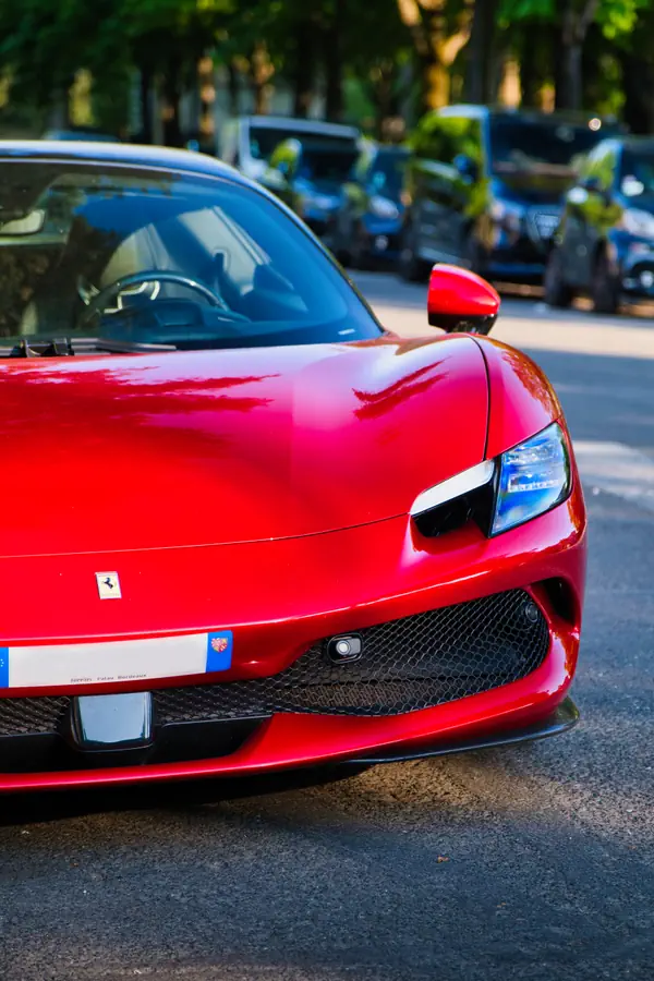 Gros plan sur l'avant d'une Ferrari 296 GTB rouge vif stationnée dans une rue ombragée de Paris.