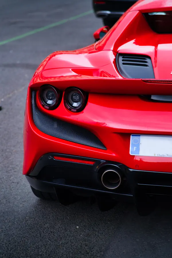 Gros plan sur l'arrière d'une Ferrari F8 Tributo rouge, montrant les feux arrière circulaires caractéristiques et la grille d'aération en fibre de carbone.