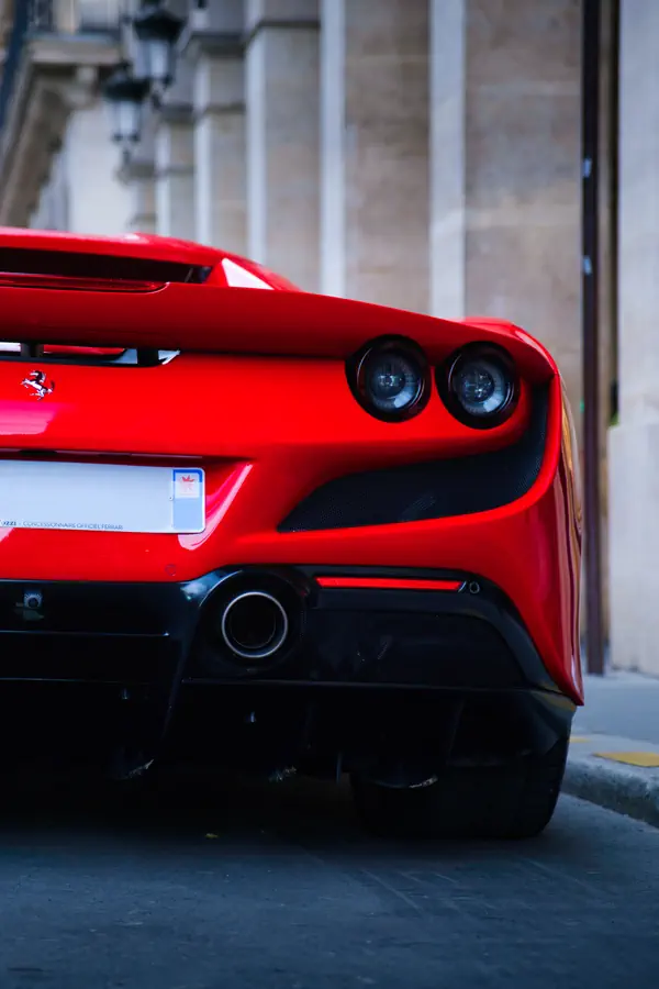Détail de l'arrière d'une Ferrari F8 Tributo rouge vif stationnée devant un bâtiment historique parisien.