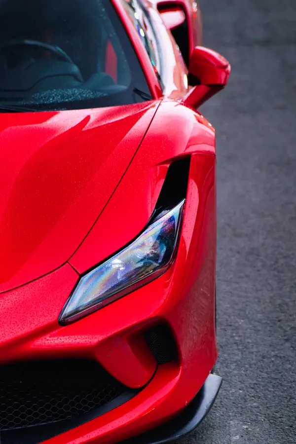 Gros plan sur le phare avant effilé d'une Ferrari F8 Tributo rouge, montrant le design agressif et sculptural de la partie avant.