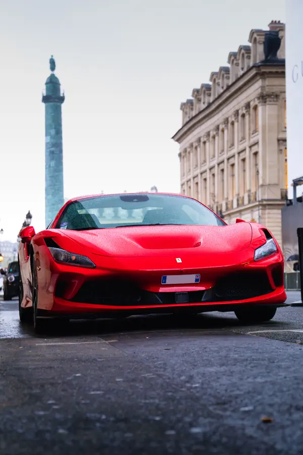Ferrari F8 Tributo rouge photographiée de face sur la Place Vendôme à Paris, avec la colonne Vendôme et un bâtiment historique en arrière-plan.