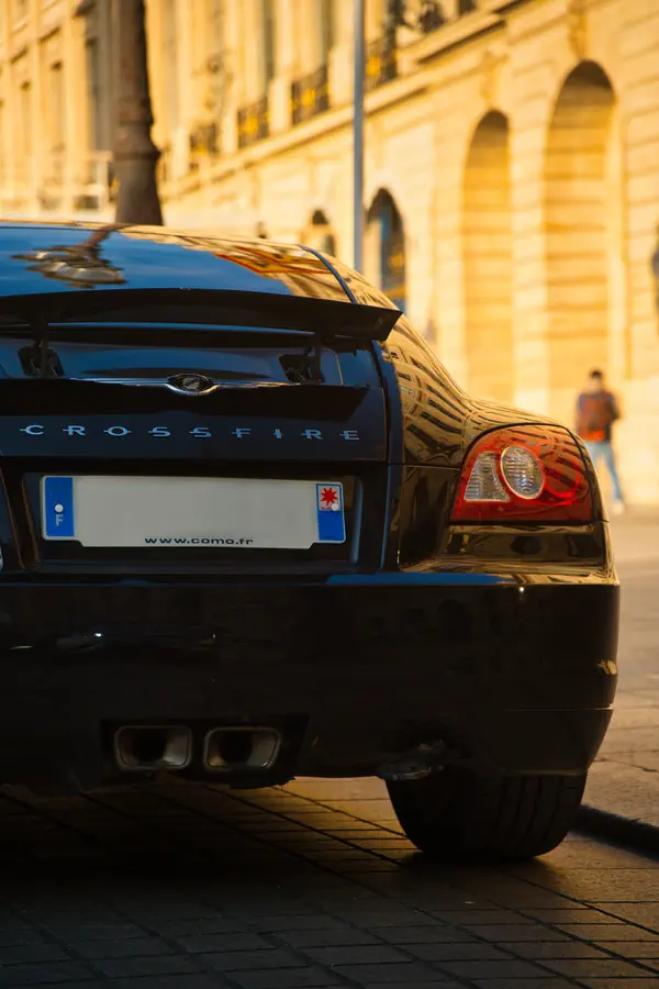 Vue arrière d'une Chrysler Crossfire noire stationnée sur la Place Vendôme à Paris, capturant le feu arrière caractéristique, le logo Crossfire et les doubles sorties d'échappement.