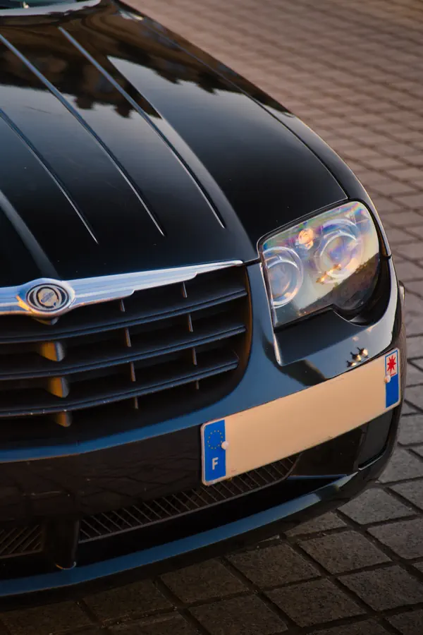 Gros plan sur l'avant d'une Chrysler Crossfire noire, montrant le phare caractéristique, la calandre avec l'emblème Chrysler et les nervures distinctives du capot.