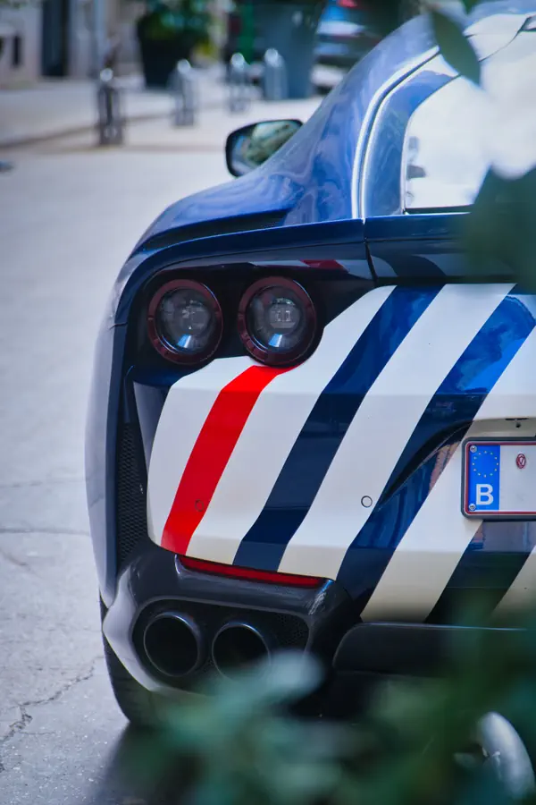 Détail de l'arrière d'une Ferrari noire décorée de bandes tricolores bleu-blanc-rouge, montrant ses feux ronds caractéristiques et ses doubles sorties d'échappement en carbone.