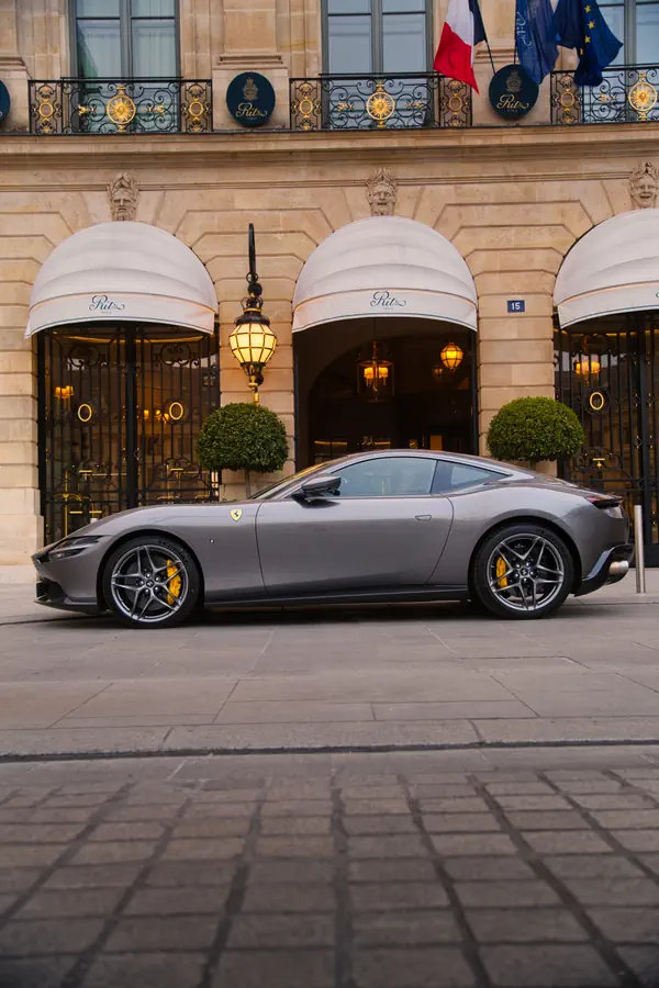 Ferrari Roma gris métallisé photographiée de profil devant l'hôtel Ritz Paris sur la Place Vendôme.