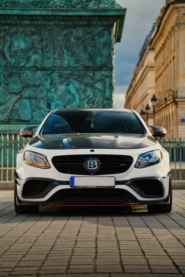 Mercedes-Benz E63 S AMG transformée par Brabus, de couleur blanche avec calandre noire et accents sportifs, photographiée de face sur les pavés de la Place Vendôme à Paris.
