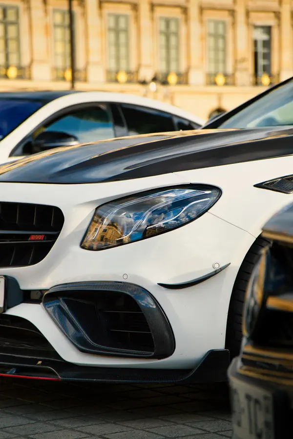 Gros plan sur l'avant d'une Mercedes-Benz E63 S AMG Brabus blanche, montrant le phare LED, la prise d'air agressive en fibre de carbone et l'insigne Brabus rouge dans la calandre.