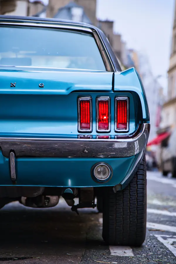 Détail de l'arrière d'une Ford Mustang classique bleu métallisé, montrant ses trois feux arrière caractéristiques en forme de bandes verticales et son pare-chocs chromé