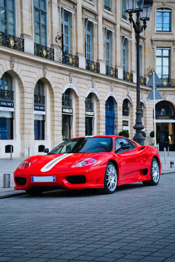 Ferrari 360 Challenge Stradale rouge vif avec bande décorative blanche et verte sur le capot, stationnée sur les pavés de la Place Vendôme.