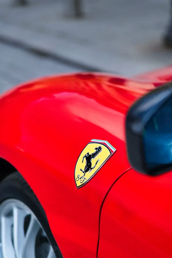 Gros plan sur l'emblématique écusson Ferrari apposé sur l'aile avant d'une Ferrari rouge éclatante.