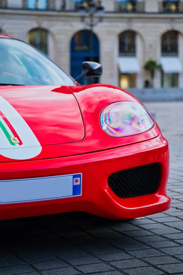 Gros plan sur l'avant d'une Ferrari 360 Challenge Stradale rouge avec phare et prise d'air latérale, arborant une bande décorative aux couleurs du drapeau italien sur le capot.