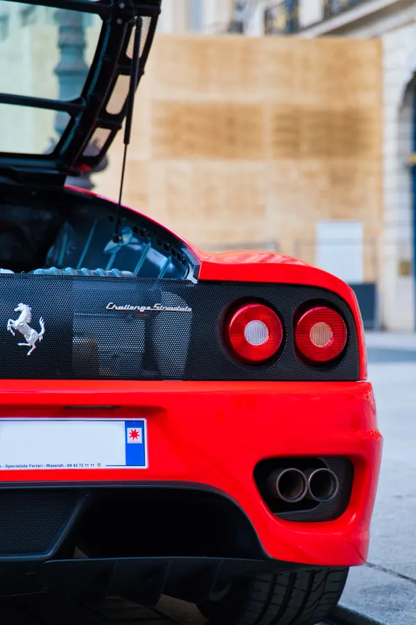 Arrière d'une Ferrari 360 Challenge Stradale rouge montrant ses feux circulaires caractéristiques, le logo du cheval cabré sur une grille noire, et les doubles sorties d'échappement.
