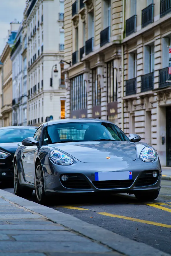 Porsche Cayman gris métallisé garé dans une rue parisienne élégante, photographié en légère contre-plongée.