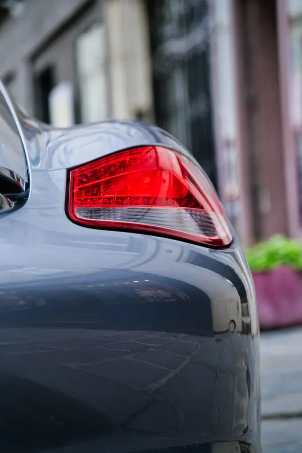 Gros plan sur le feu arrière rouge d'une Porsche Cayman gris métallisé, montrant le design élégant et profilé du panneau de carrosserie.