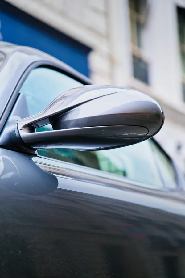 Gros plan sur le rétroviseur extérieur aérodynamique d'une Porsche Cayman gris métallisé, montrant sa forme profilée et sa finition brillante.