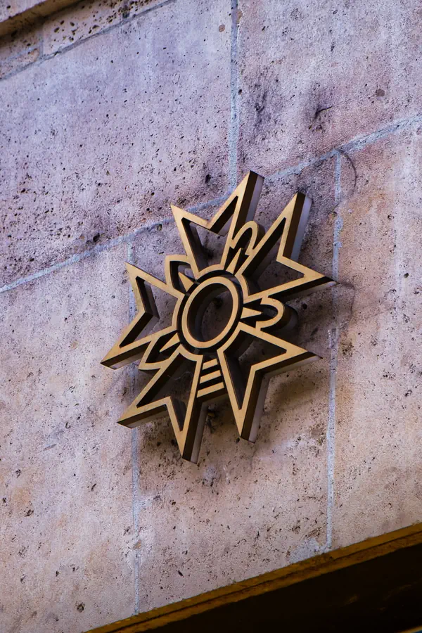 Motif décoratif en forme d'étoile dorée en relief, fixé sur un mur en pierre de taille, créant un contraste graphique entre le métal brillant et la texture brute de la pierre